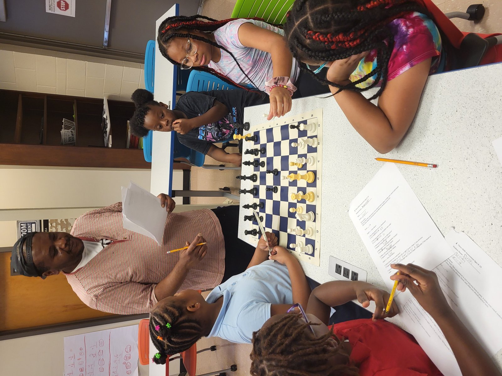 Coach Corbin teaching a chess lesson to a group of kids around the board